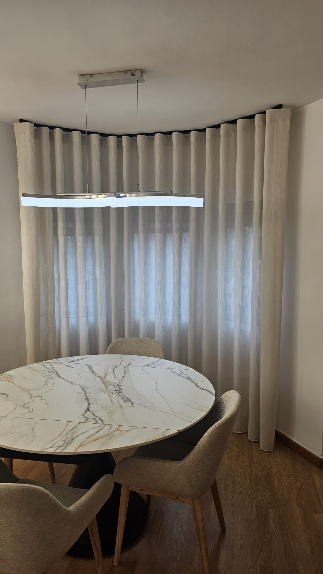 Cortina de ondas en un ventanal curvo, sobre una mesa de comedor de mármol
