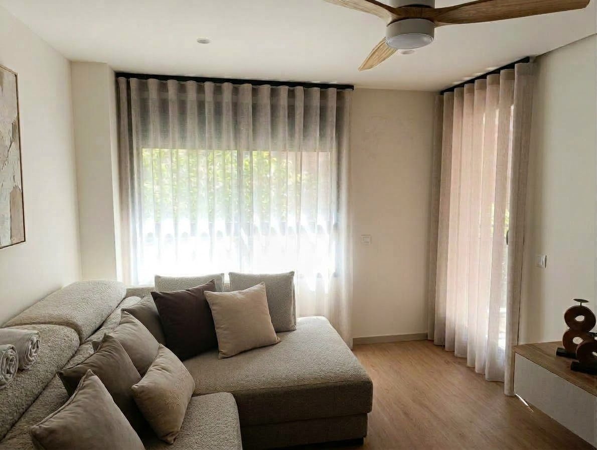 Salón con visillo ondulado y cortina de lino junto a la puerta de la terraza