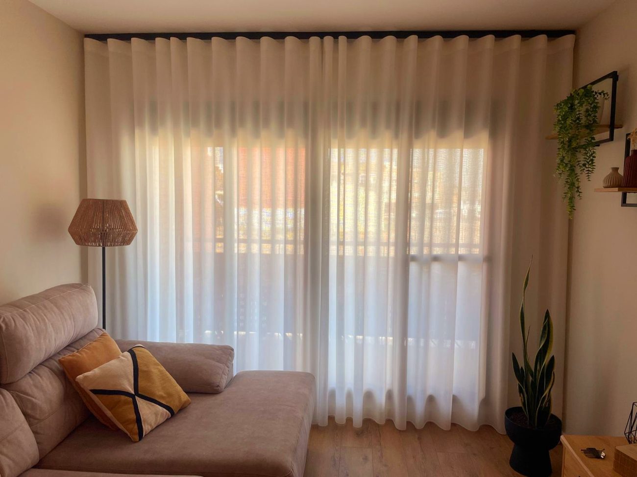 Salón con visillo ondulado blanco y lámpara de rafia