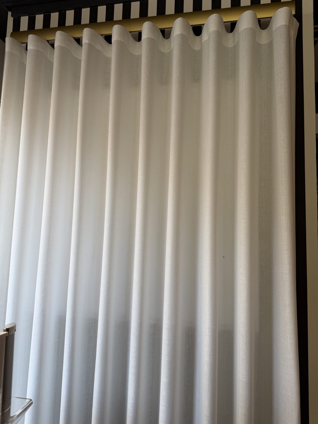 Detalle de un visillo ondulado de lino blanco en un riel dorado, en el estudio