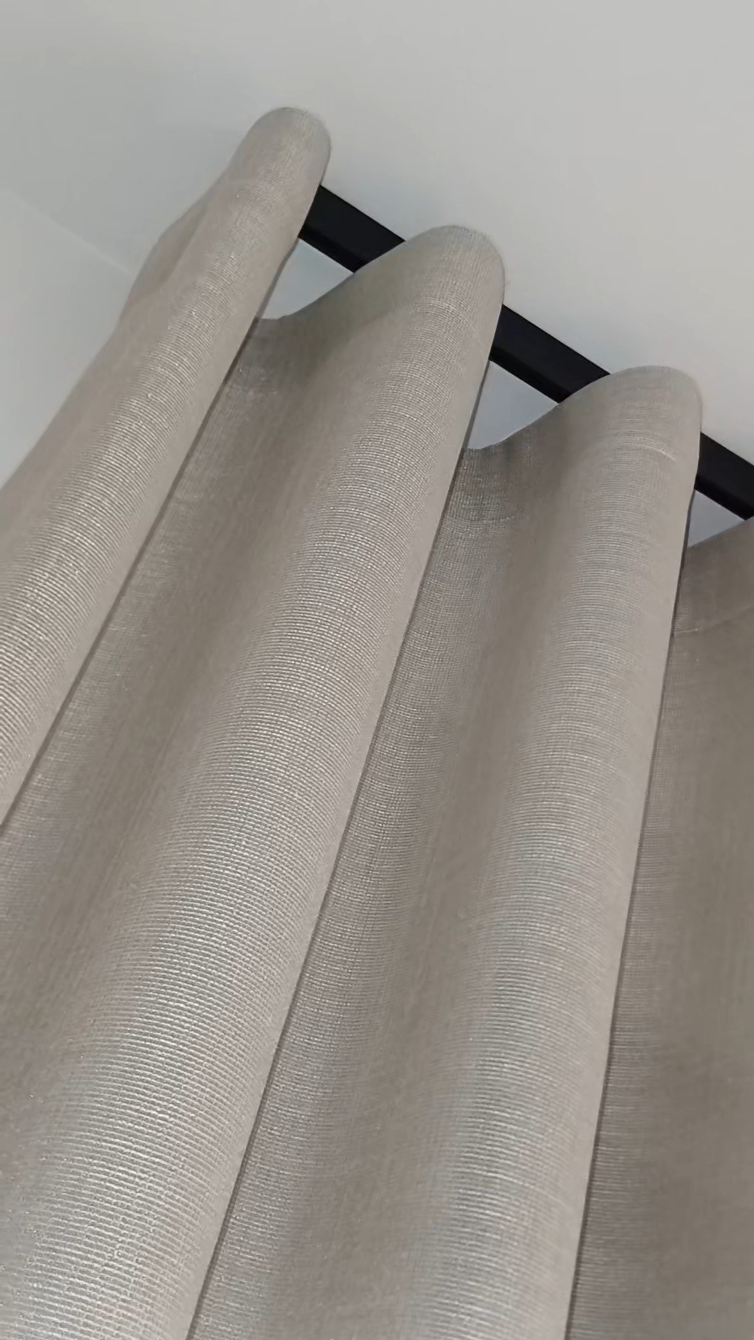 Detalle de una cortina de lino con las ondas colgadas del riel negro